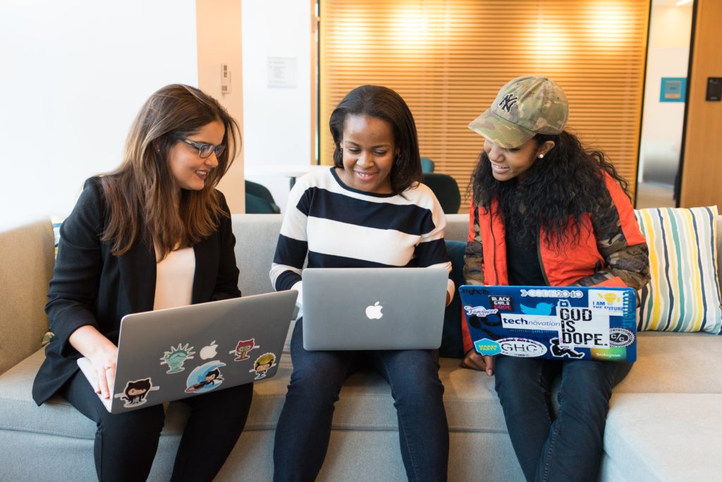 Imagem de 3 moças em um sofá com laptops no colo